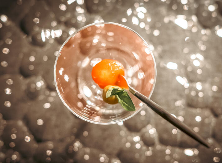 Cherry tomato opening bite presented on a skewer over a reflective glass plate.